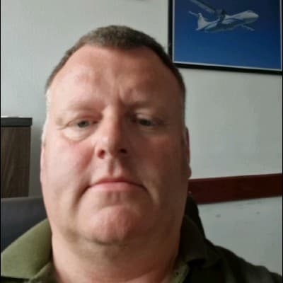 Middle-aged man in a green polo shirt with a framed airplane picture behind him.