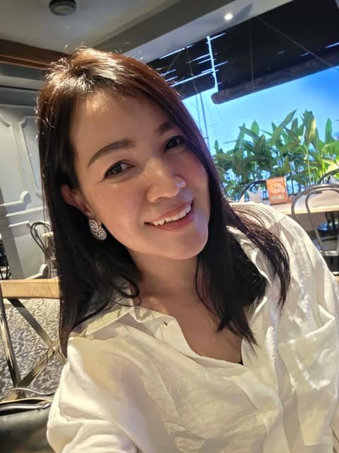 Smiling woman with dark hair wearing a white shirt and sparkly earrings in a restaurant.